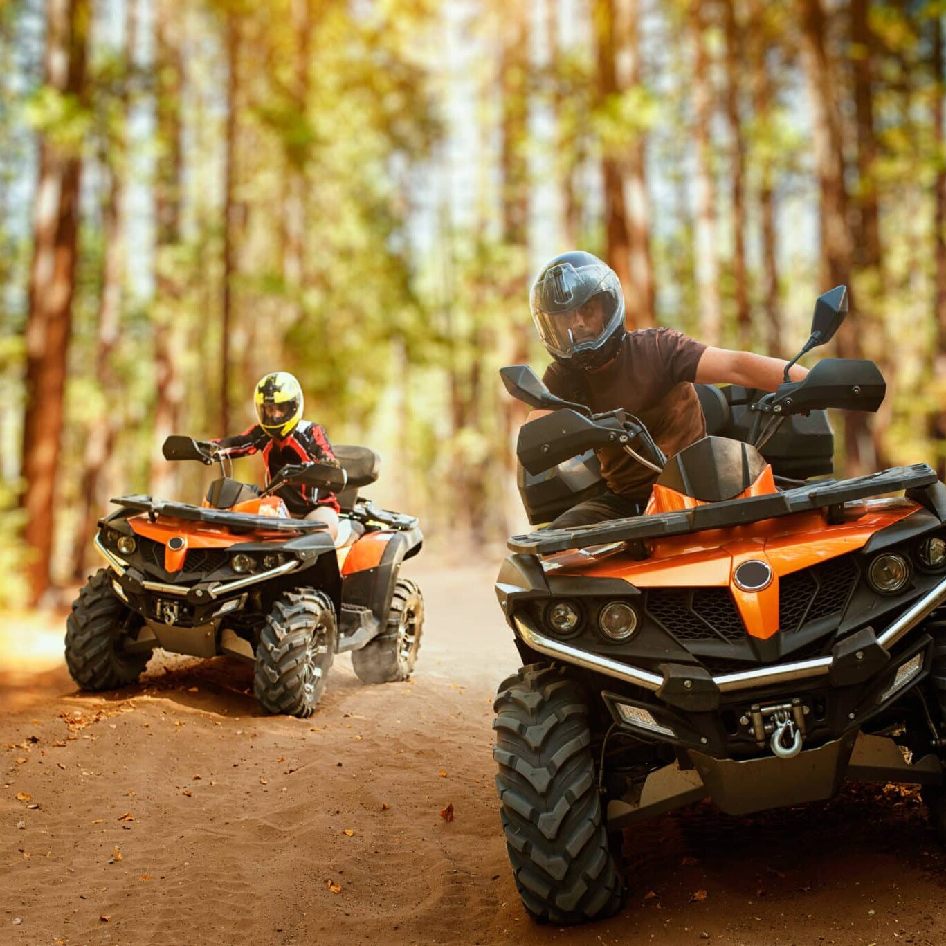 Two atv riders in helmets, speed race in forest, front view. Riding on quad bike, extreme sport and travelling, quadbike offroad adventure